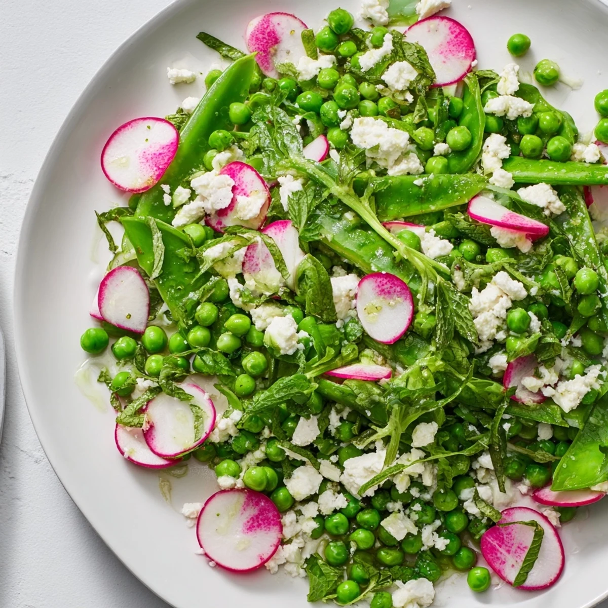 A close-up of Spring Pea Salad with Radishes and Feta, topped with crumbled cheese and vibrant sliced radishes.
