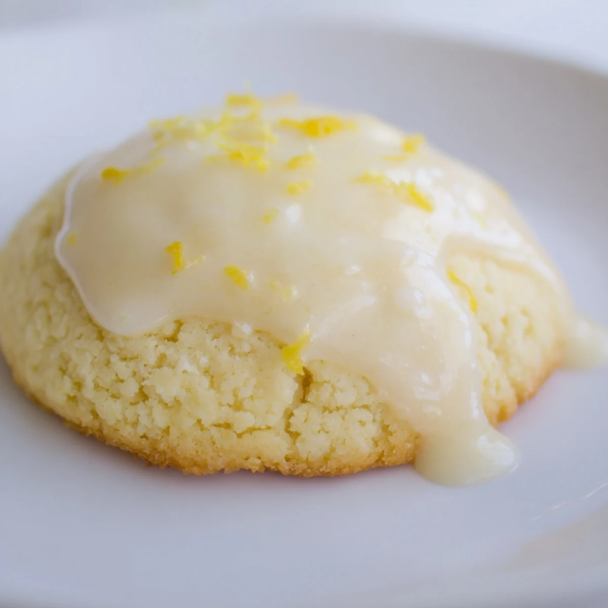 A close-up of Lemon Ricotta Cookies with Glaze, where tangy glaze drips over soft, pale-yellow cookies dusted with lemon zest.