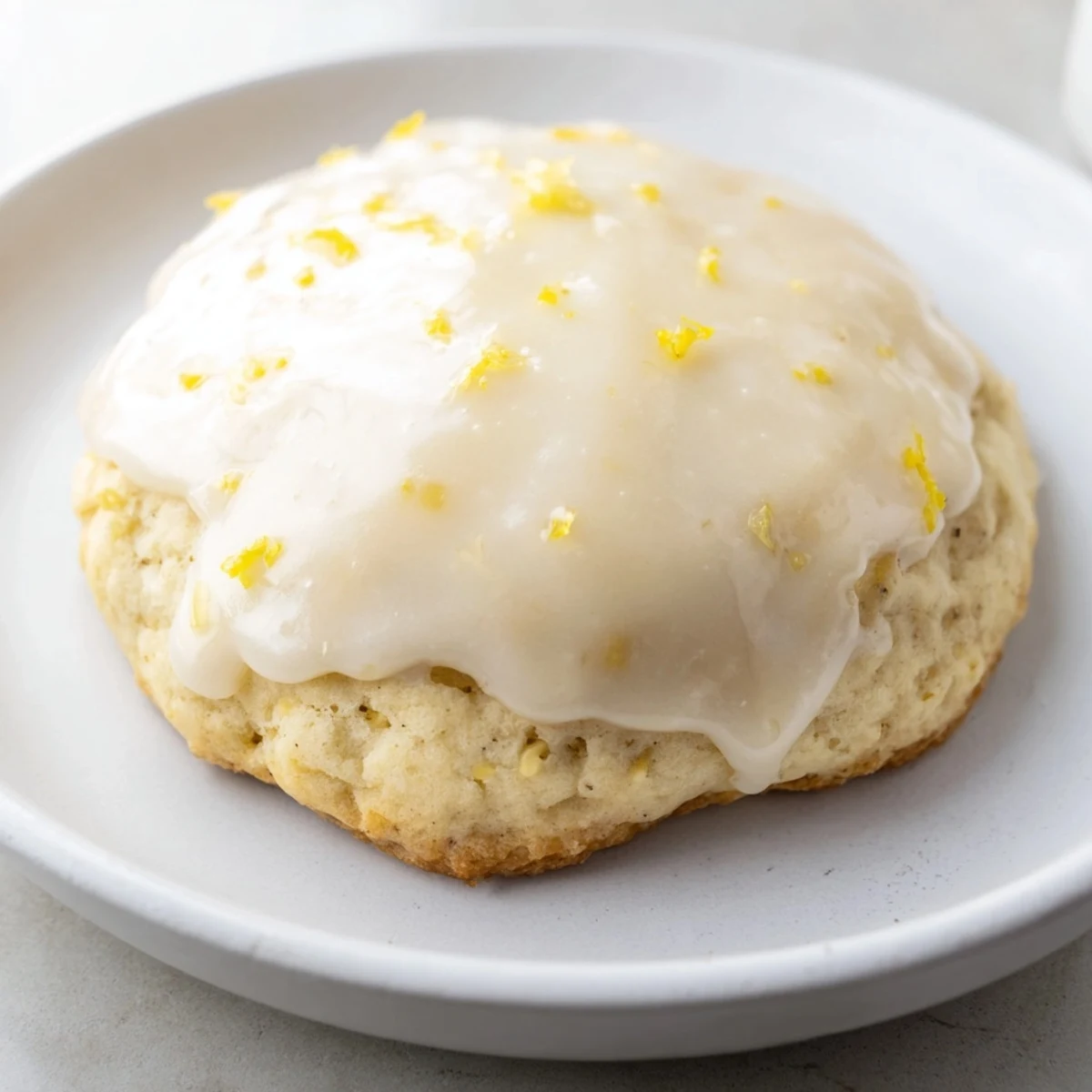 Freshly baked Lemon Ricotta Cookies with Glaze on a white ceramic plate, showing moist, cake-like centers and a glossy, sweet lemon drizzle.