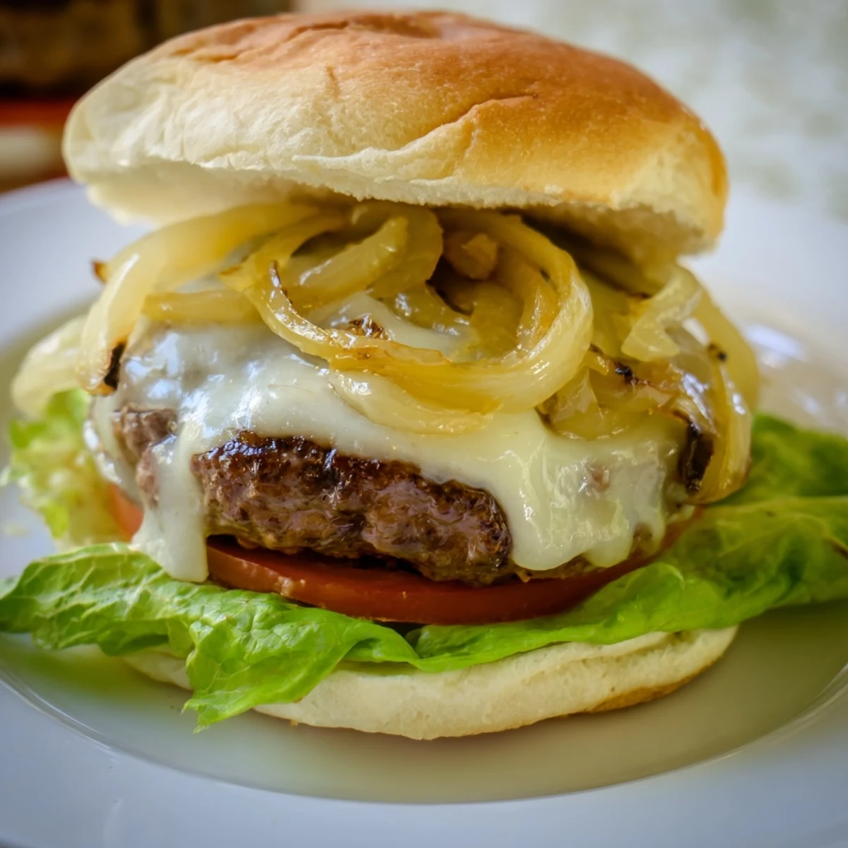 A close-up of a Beef Burger with Caramelized Onions and Swiss cheese on a toasted bun, with lettuce and tomato visible.