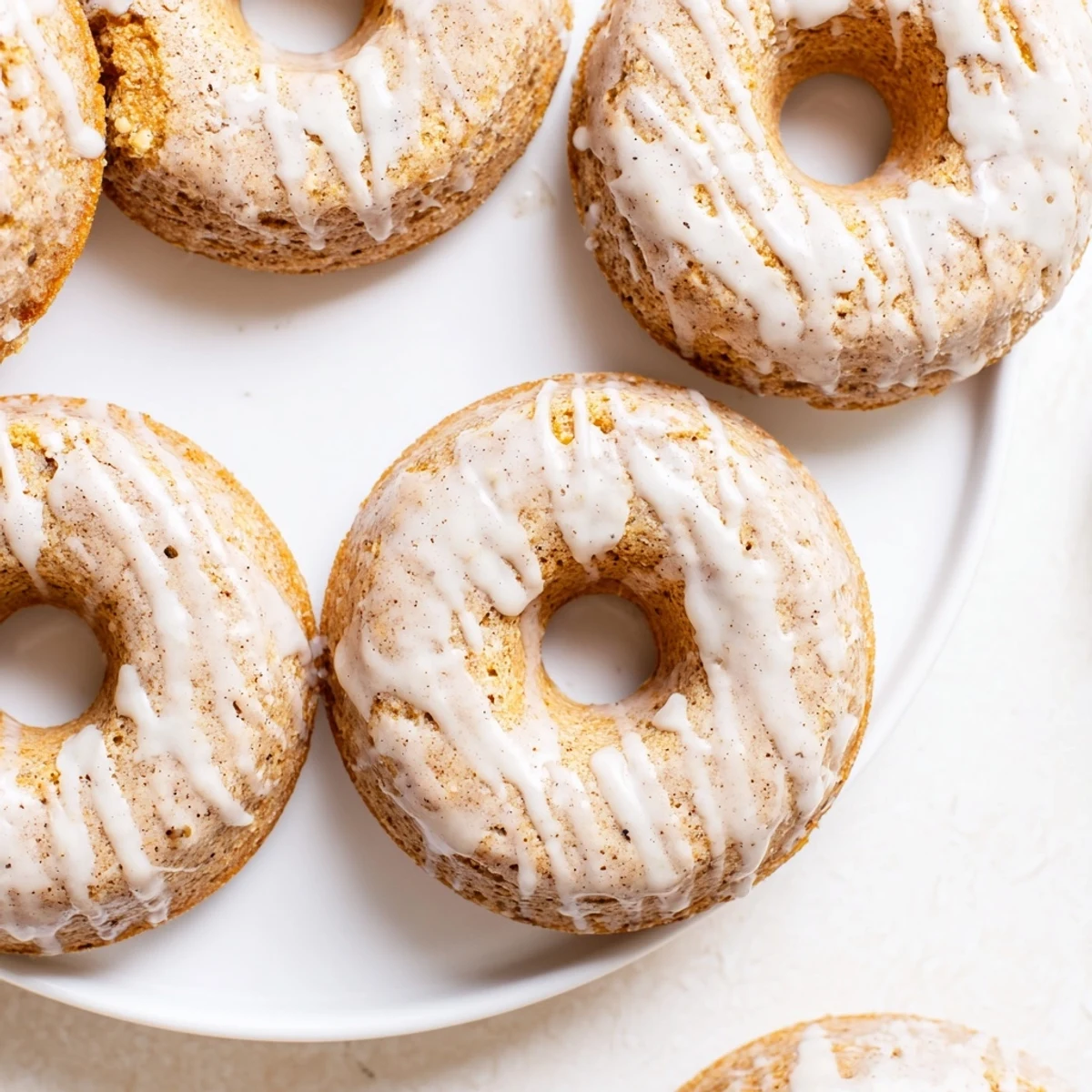 Glazed Baked Banana Bread Donuts arranged on a white plate, with a drizzle catching the light.