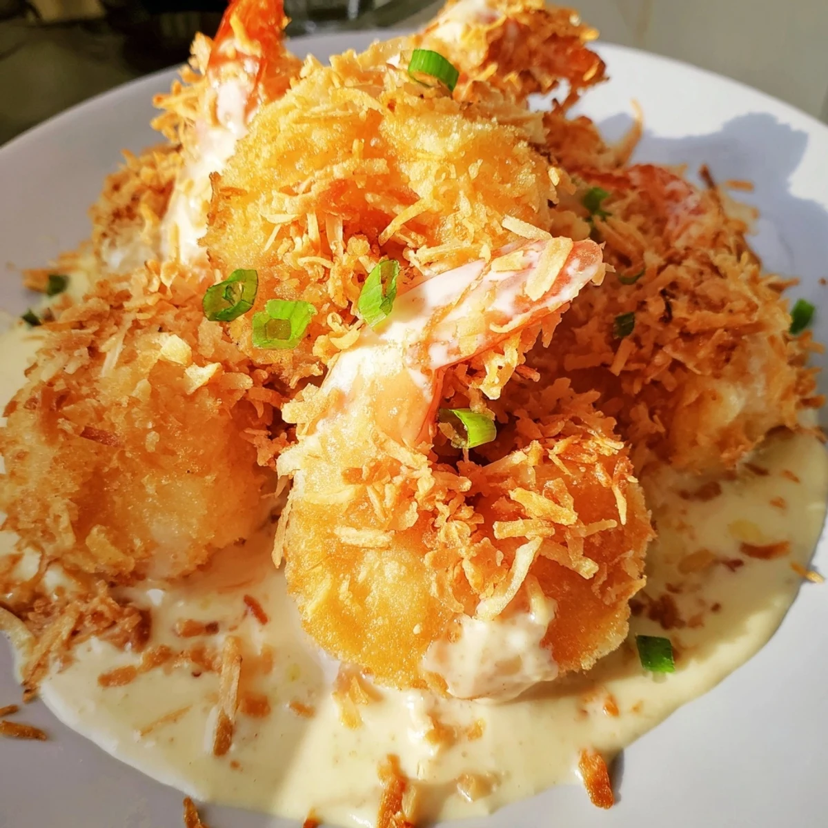 Crispy battered Chinese Coconut Shrimp glistening in creamy coconut sauce with toasted coconut garnish on a plate.  