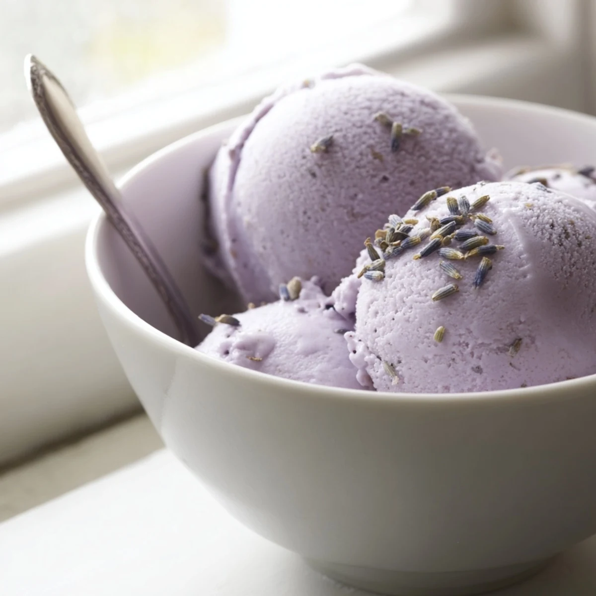 Lavender Ice Cream is served in a rustic ceramic bowl with a shortbread cookie, highlighting the creamy purple swirls.
