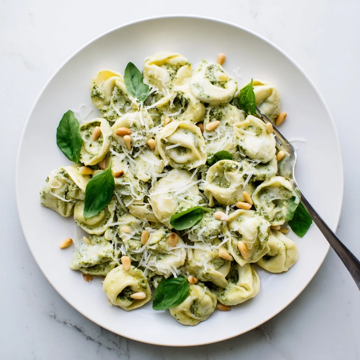 Pesto Alfredo Tortellini is plated beside a glass of Pinot Grigio, perfect for a weeknight Italian-American dinner.