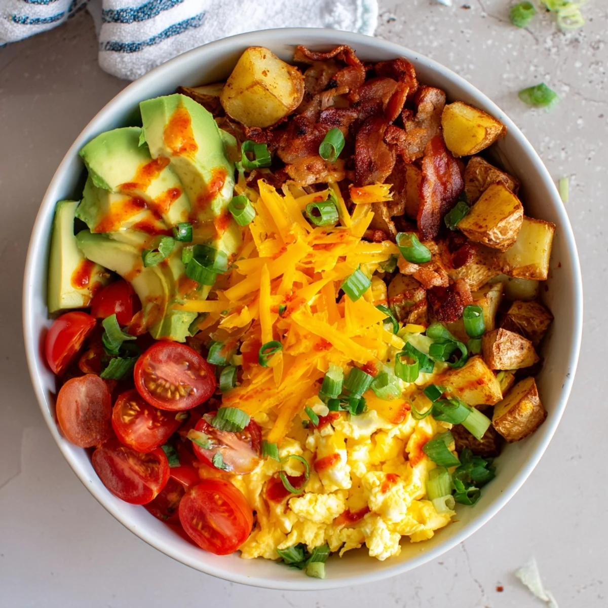 The Loaded Breakfast Bowl features diced avocado, halved cherry tomatoes, and sliced green onions arranged over roasted potatoes and eggs.