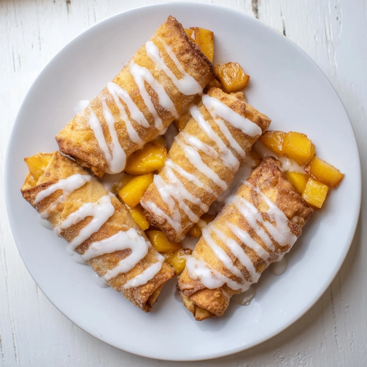 Golden peach cobbler egg rolls drizzled with sweet vanilla glaze on white plate