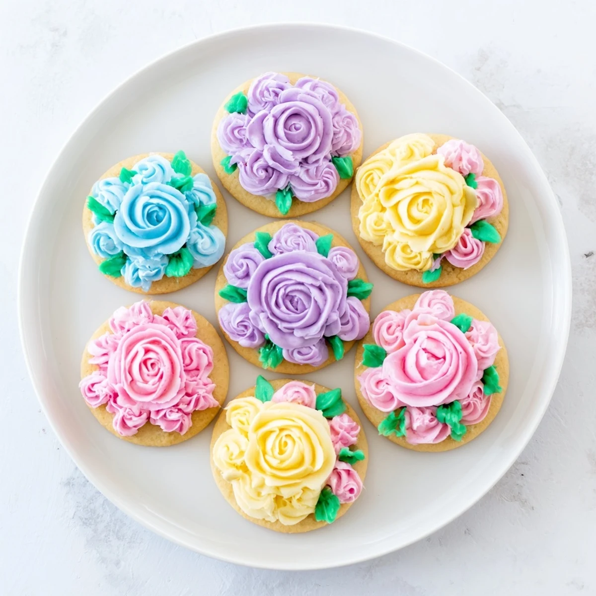 Decorated buttercream flower cookies featuring delicate rosettes and green leaves on round sugar cookies