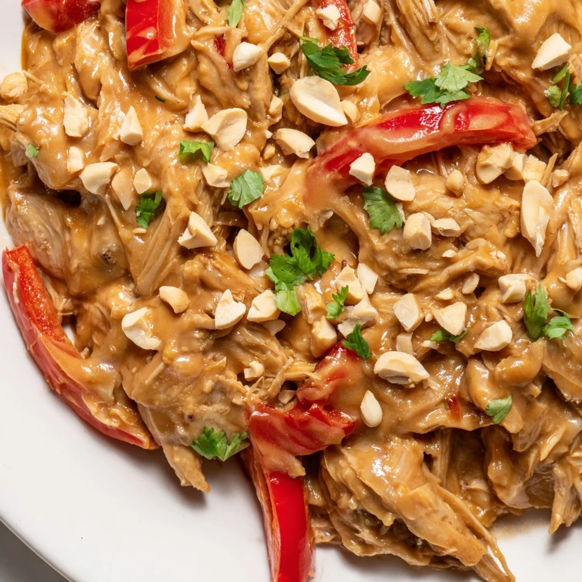 Golden slow cooker peanut chicken garnished with crushed peanuts and fresh cilantro over fluffy white rice