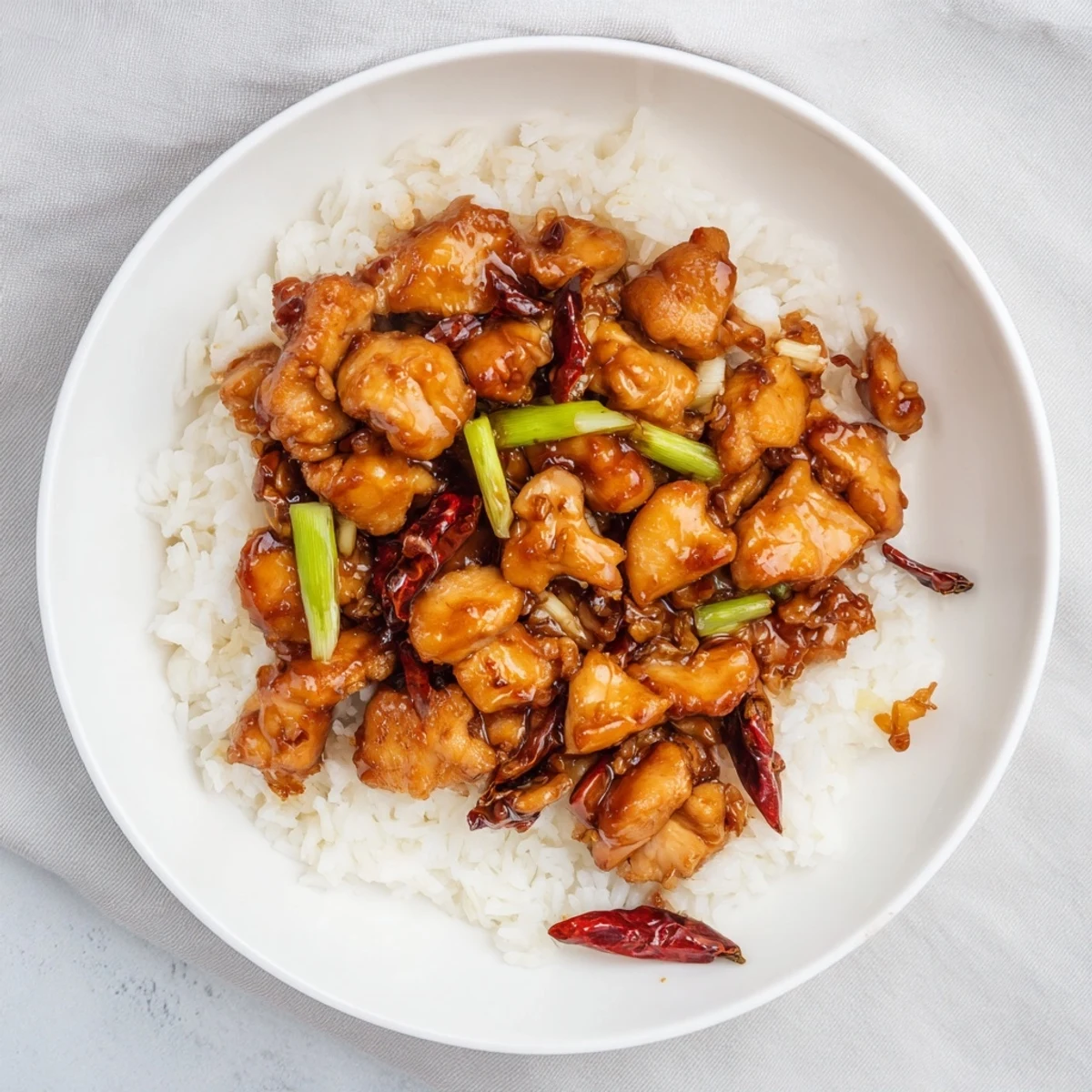 Golden Mongolian chicken pieces coated in thick brown soy garlic glaze with fresh green scallions over white rice