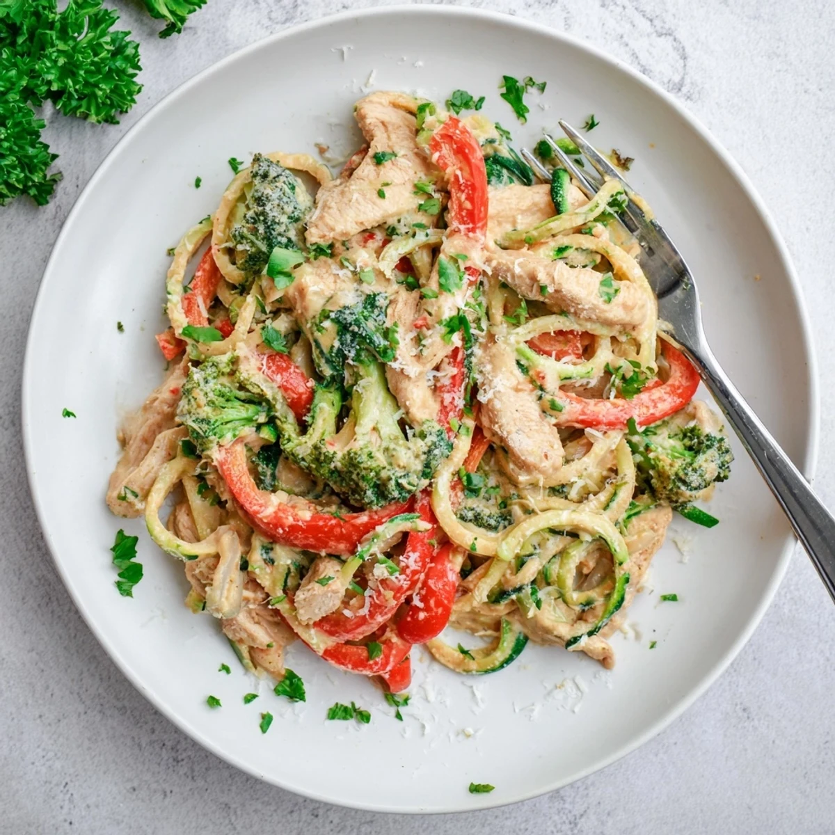 Lighter protein-packed zucchini noodle Alfredo featuring spiralized zucchini, colorful vegetables, and golden chicken in a velvety garlic cream sauce