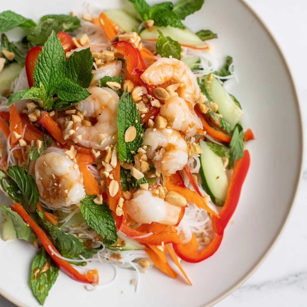 Vibrant deconstructed spring roll salad with rice noodles, colorful crunchy vegetables, succulent shrimp, and chopped peanuts topped with spicy ginger dressing