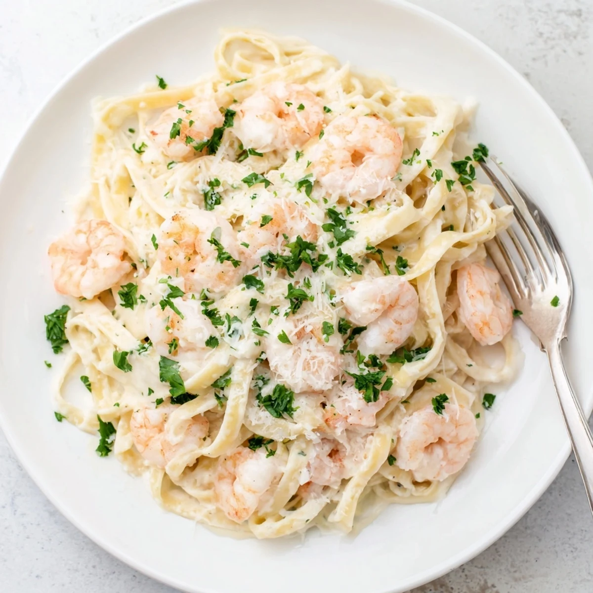 Tender shrimp tossed with fettuccine noodles in rich white Parmesan cream sauce on a white plate