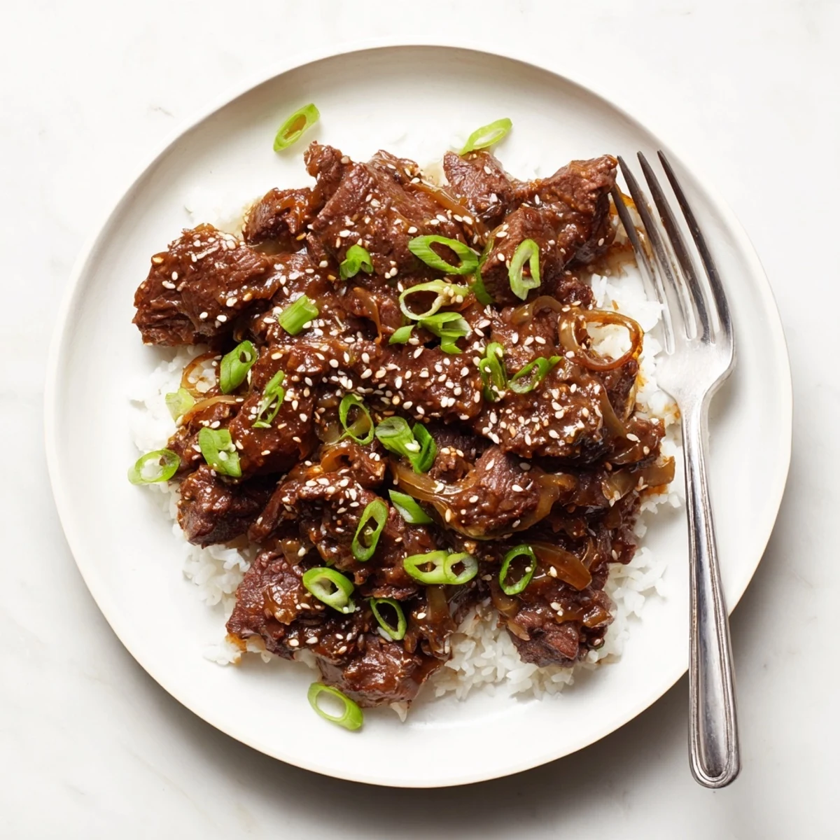 Tender shredded slow cooker Korean beef draped in rich glossy dark sauce over fluffy white rice