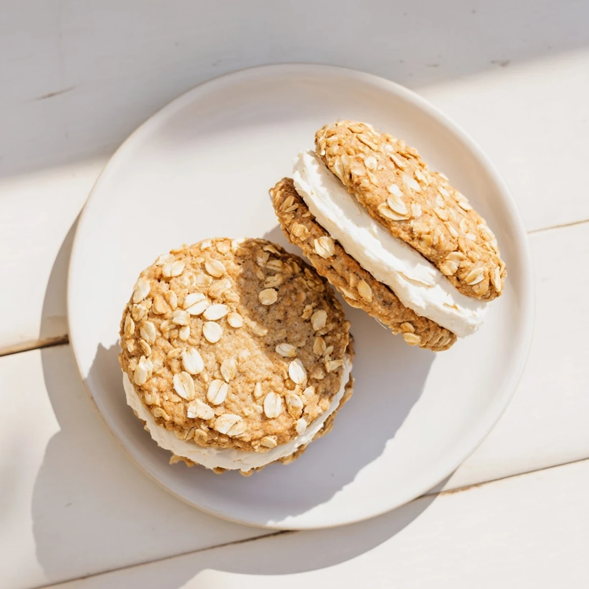 Close-up of chewy oatmeal cookie sandwich filled with thick white cream filling on a white plate