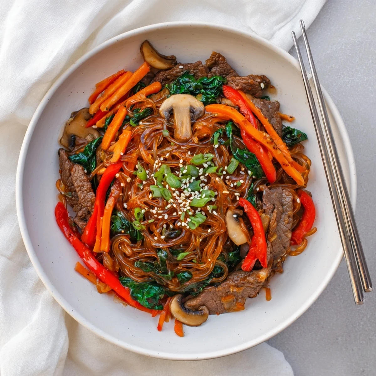 Savory Korean beef noodles stir-fried with crisp bell peppers, carrots, mushrooms, and spinach in a rich sweet and spicy glaze