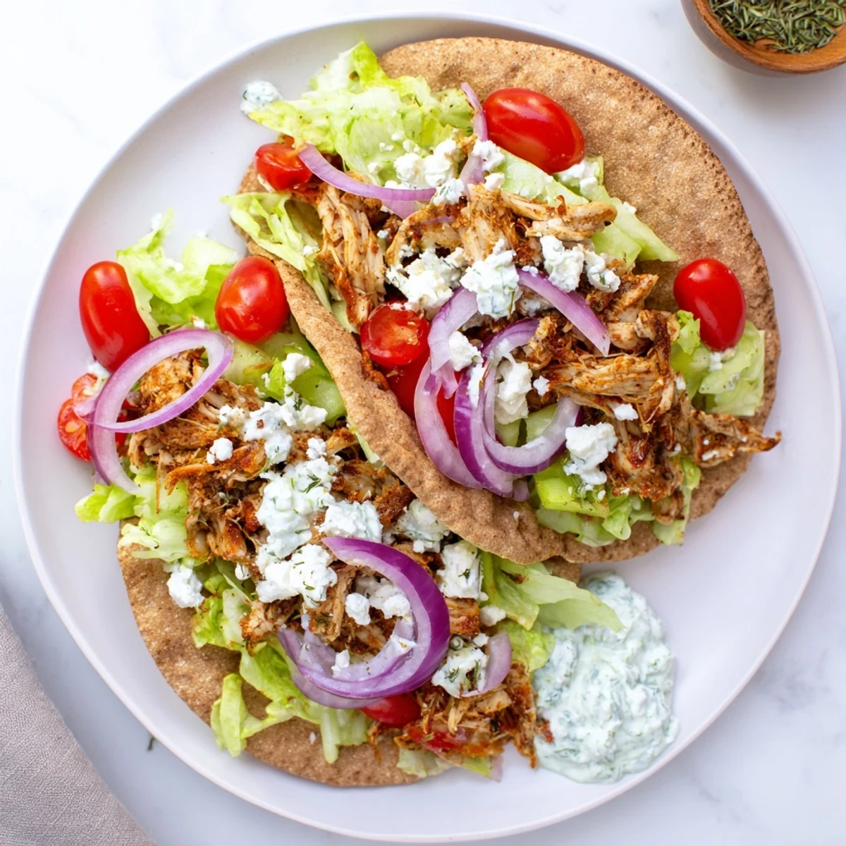 Handheld Crockpot Greek chicken pita overflowing with seasoned meat feta cheese and cooling homemade tzatziki dressing