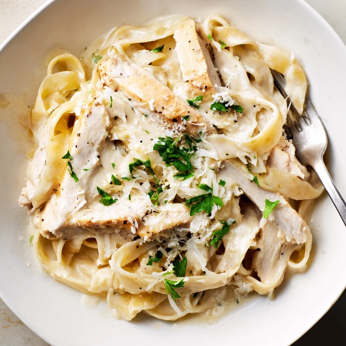 Creamy garlic parmesan chicken pasta plated with sliced chicken breast and fresh parsley garnish