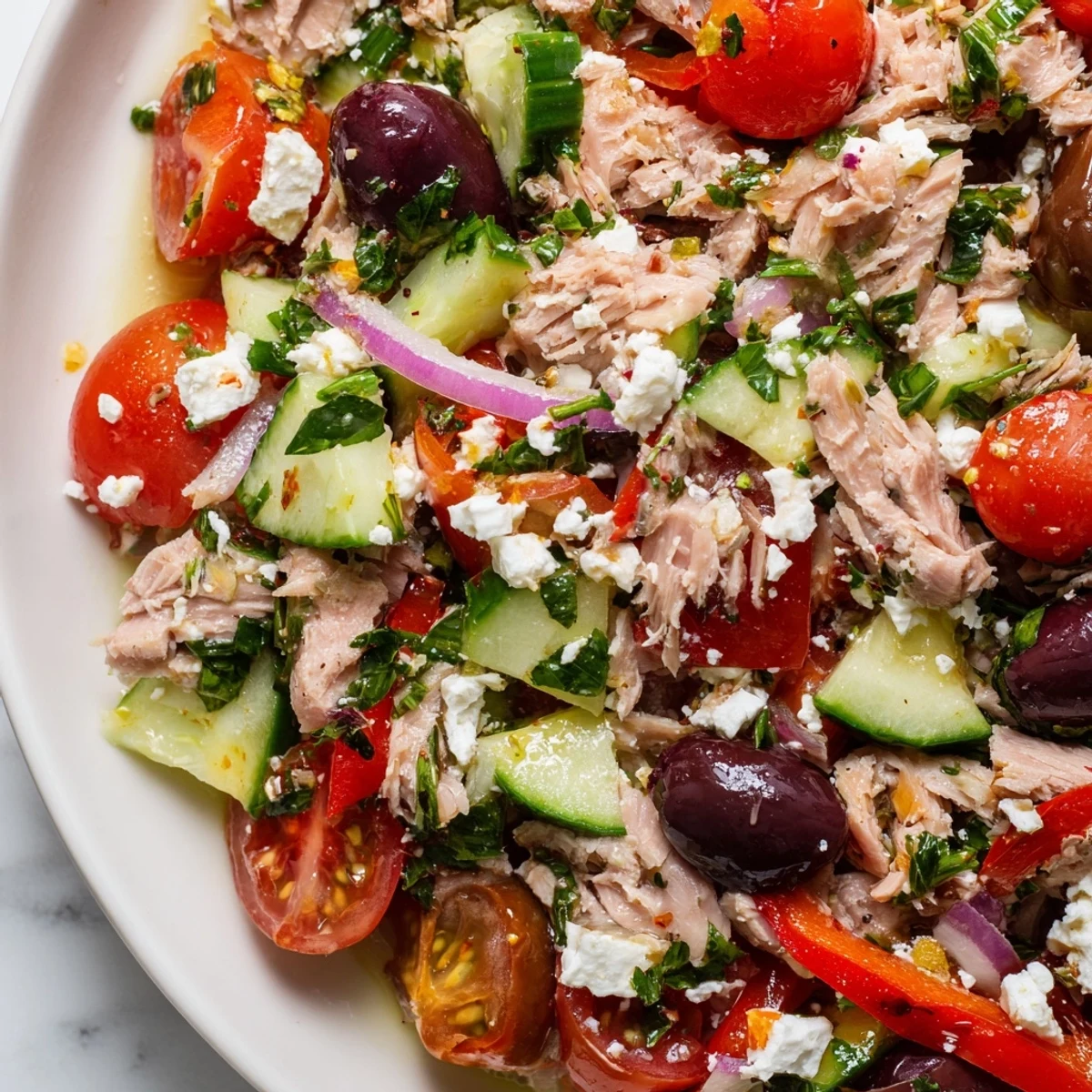 Colorful Mediterranean tuna salad bowl with fresh vegetables, olives, and lemon drizzle on white background