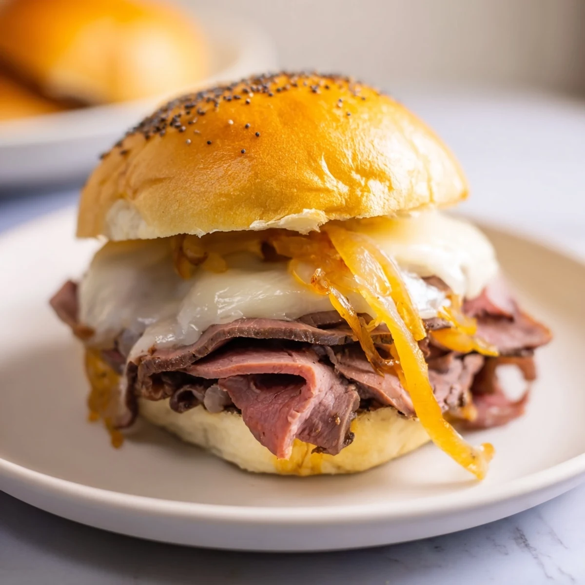 Baked party sliders featuring cheesy roast beef layers with poppy seed tops and dark beef broth