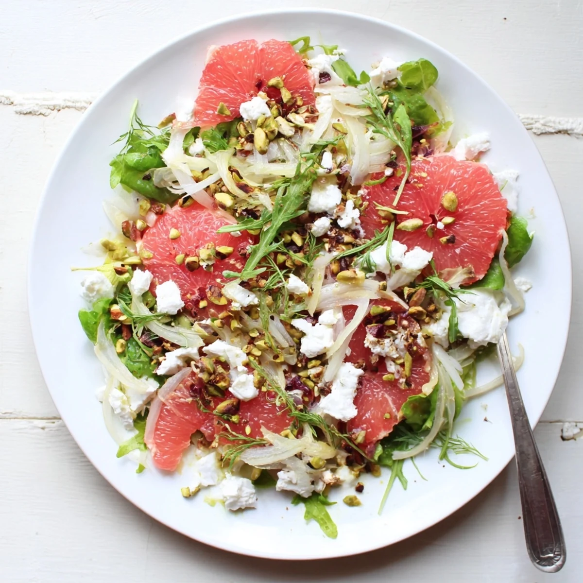 Fresh grapefruit goat cheese fennel salad with pink citrus segments, creamy cheese crumbles, and crisp arugula on white platter