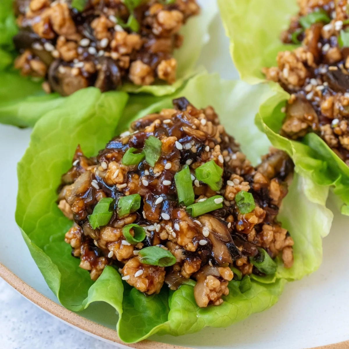 Savory ground chicken mixture spooned into fresh green lettuce leaves garnished with sesame seeds