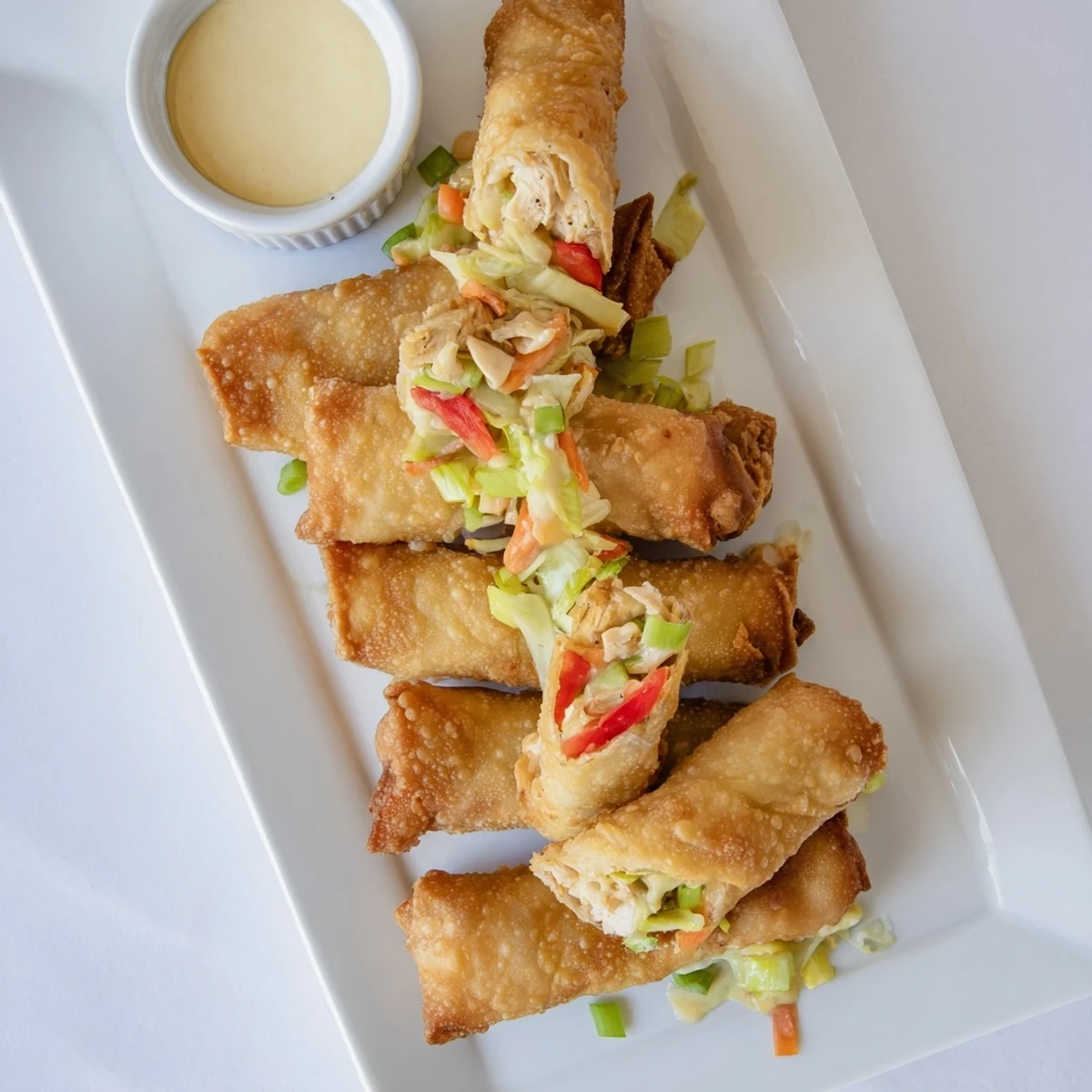 Spicy Cajun chicken Voodoo Egg rolls arranged on a serving platter with small ramekin of red dipping sauce