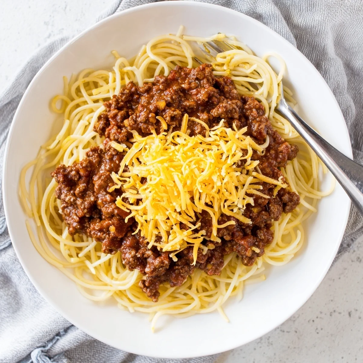 Homemade Cincinnati Chili served three-way style over pasta with a blanket of melted cheddar cheese topping