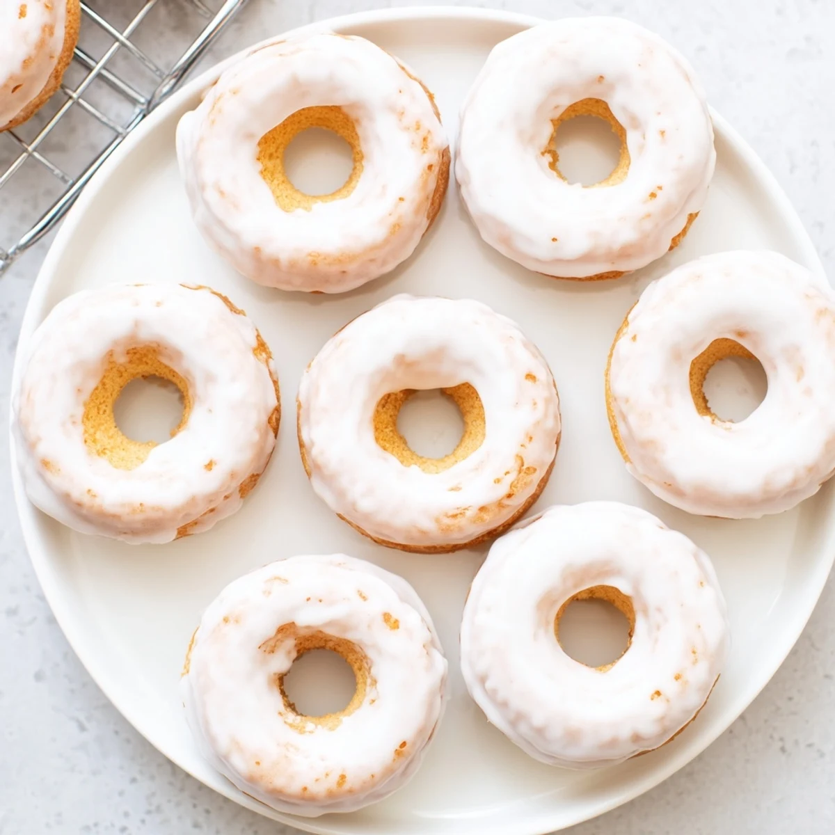 Freshly baked Greek yogurt cake donuts cooling on a wire rack, with a glossy white glaze dripping down