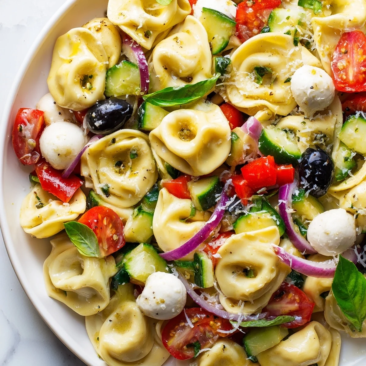 Creamy cheese tortellini salad tossed with crisp vegetables and herbs in bowl