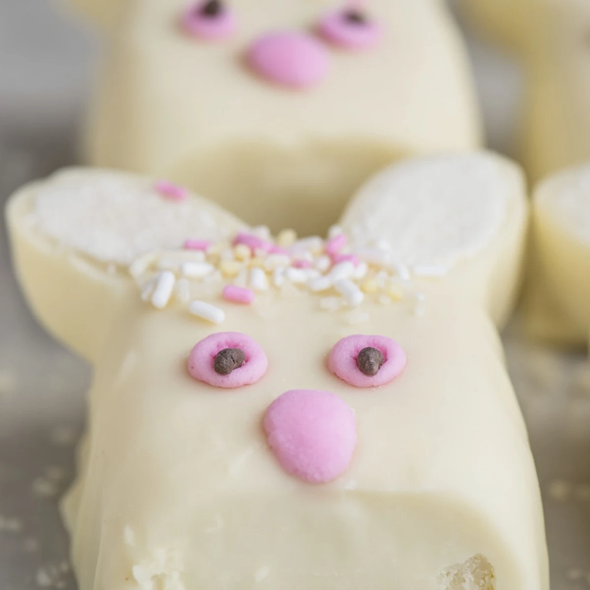 Creamy white chocolate bunny cakesicles decorated with pink ears and colorful spring sprinkles