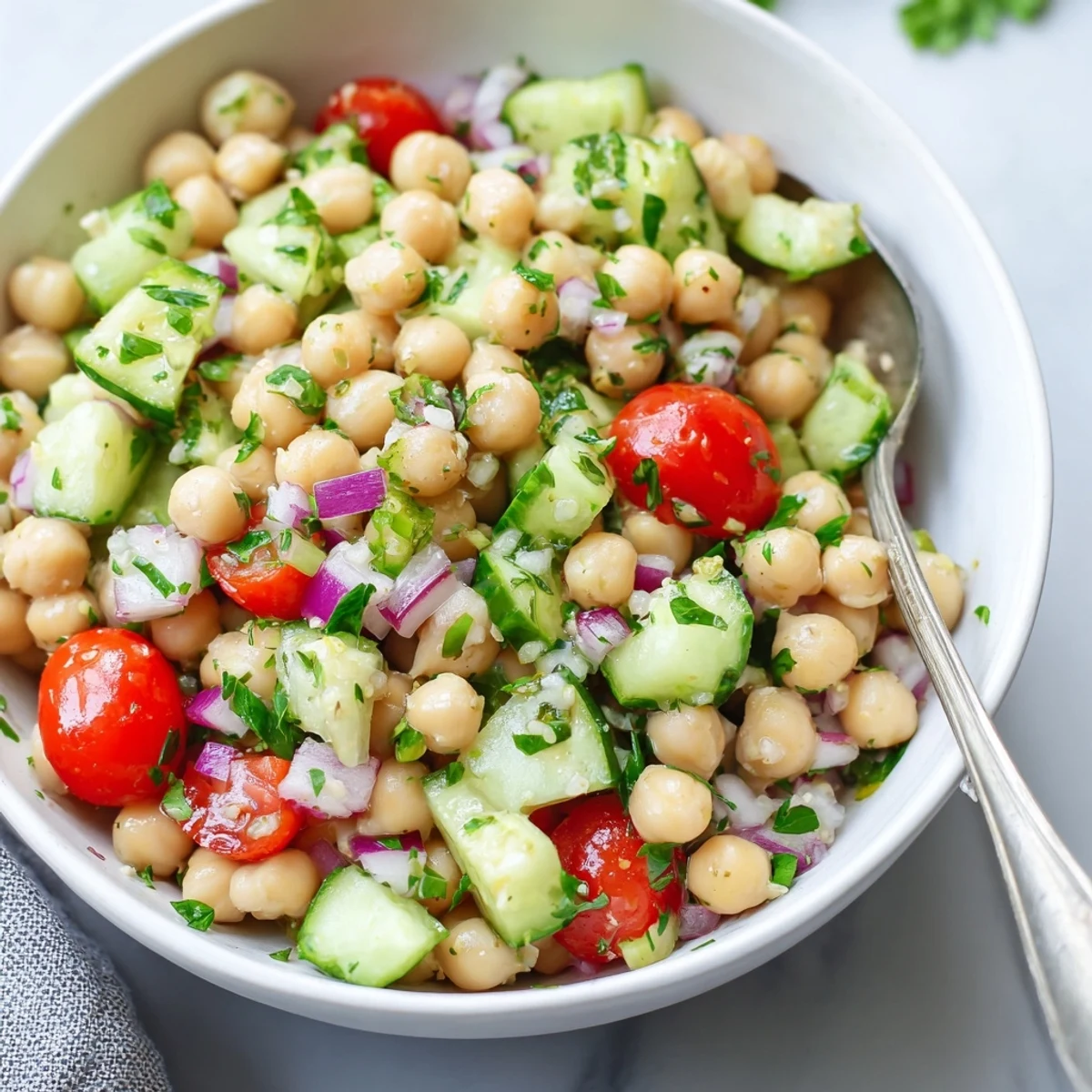 Chickpea cucumber salad in a white bowl with fresh herbs and lemon dressing
