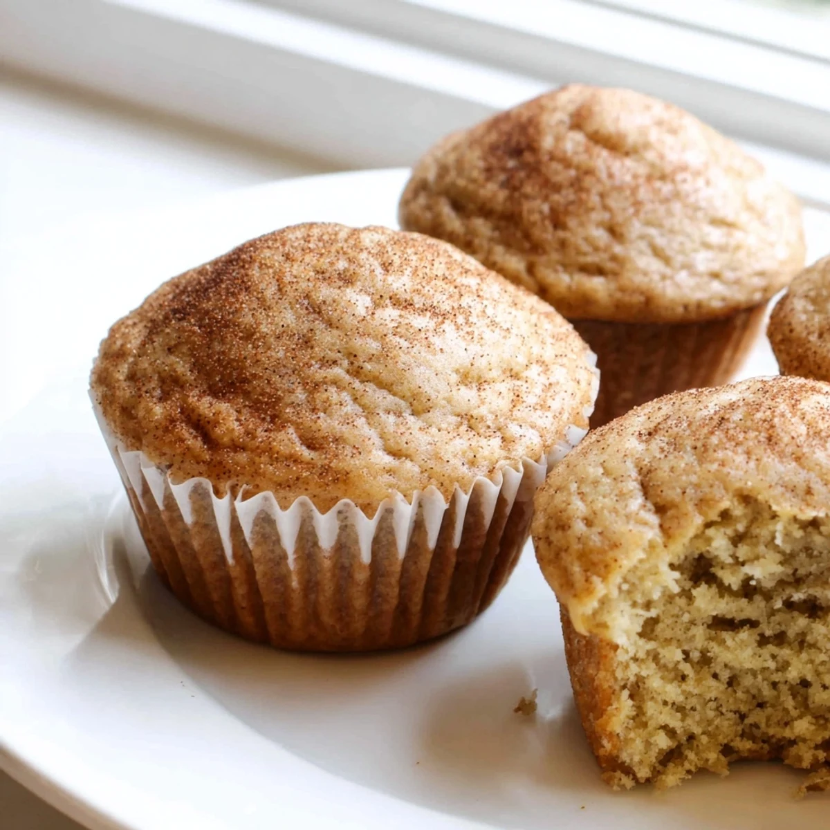 Soft banana muffins arranged on a rustic plate beside ripe bananas and melted butter.