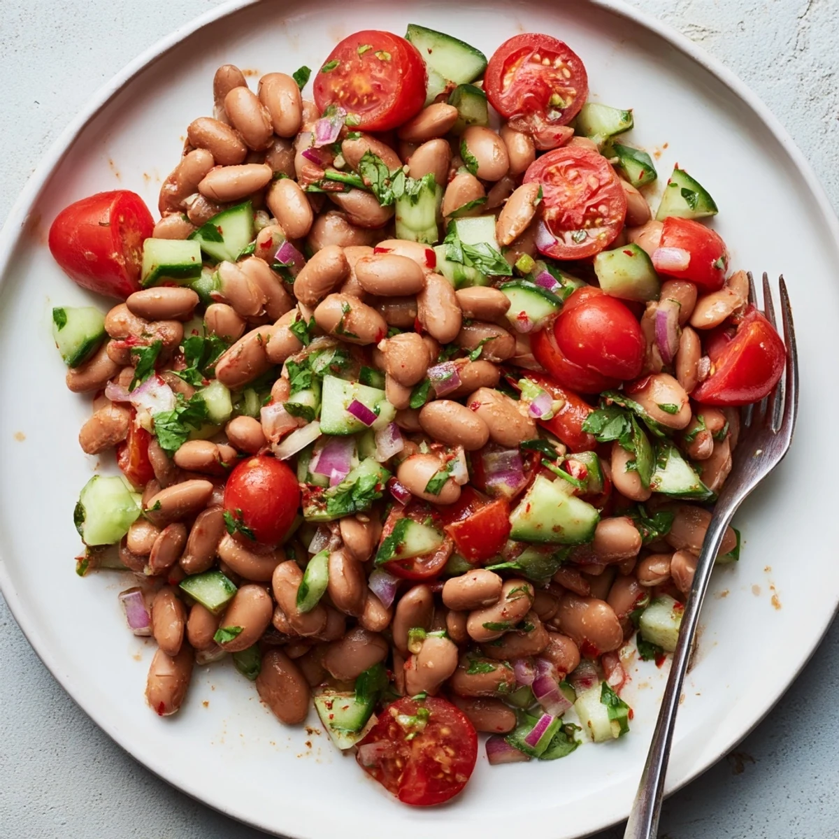 Colorful pinto bean salad in a bowl with tomatoes, cucumber, and cilantro