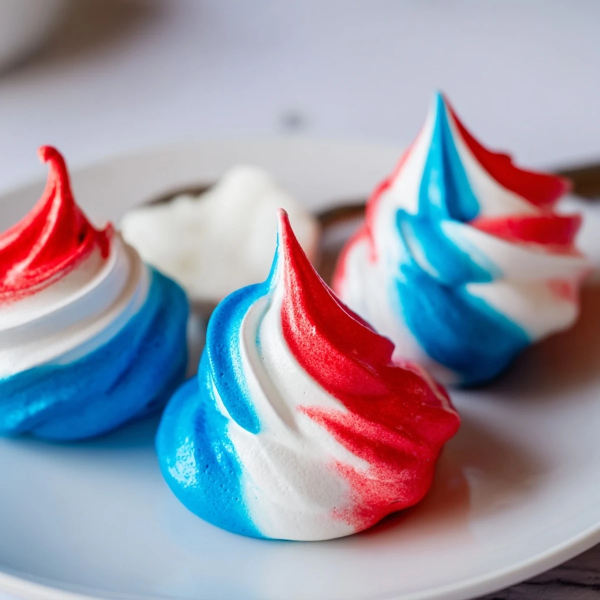 Patriotic Meringue Kisses on parchment, crisp shells with red, white, and blue swirls.