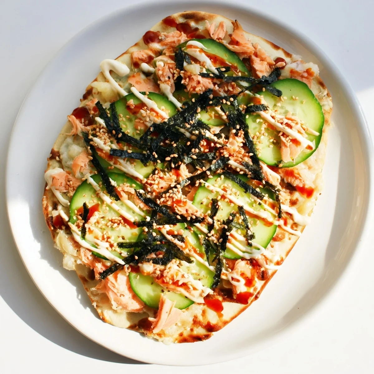 Golden salmon sushi bake flatbread pizza topped with fresh avocado, cucumber, and spicy sriracha mayo drizzle
