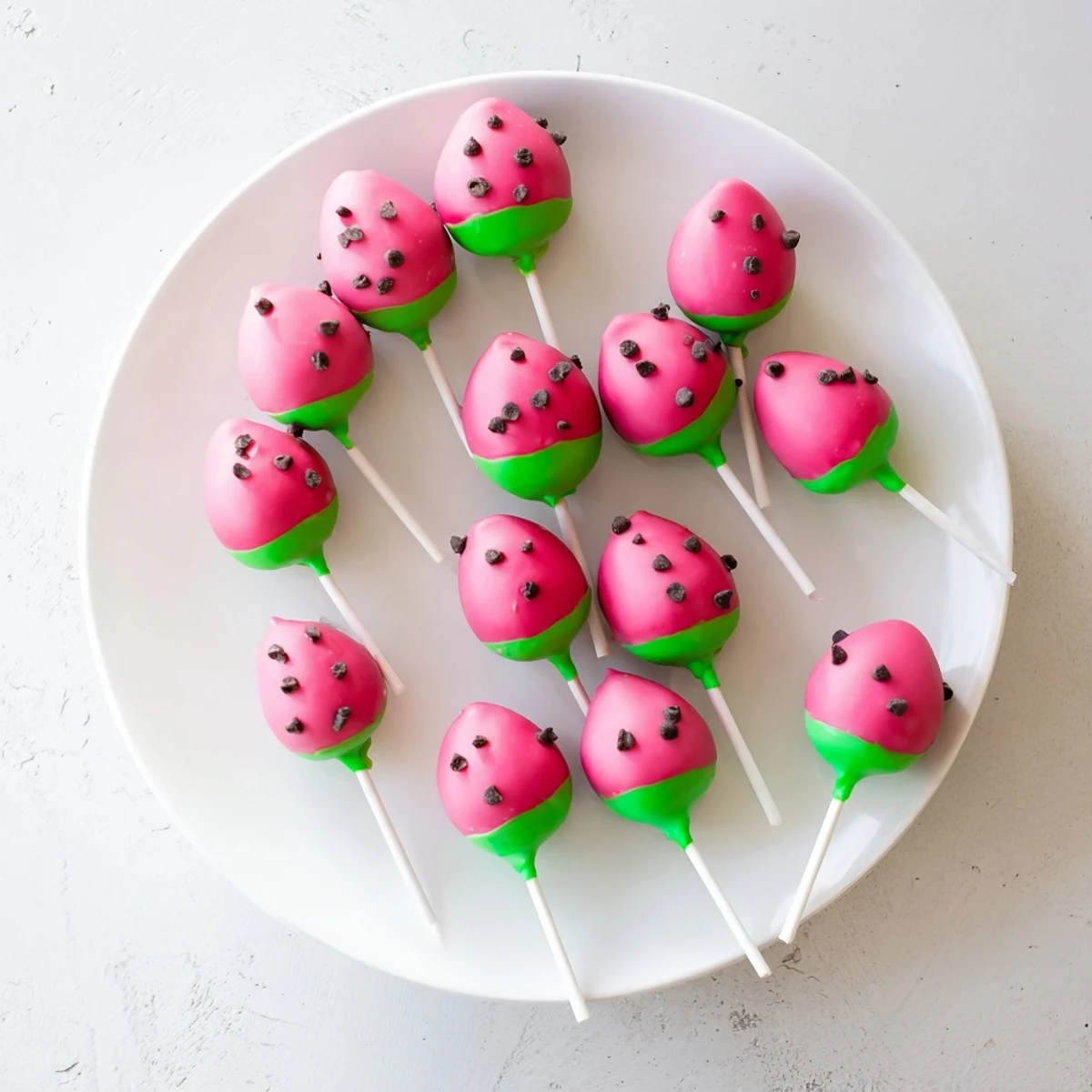 Bite-sized watermelon cake pops decorated with mini chocolate chips and colorful candy melts