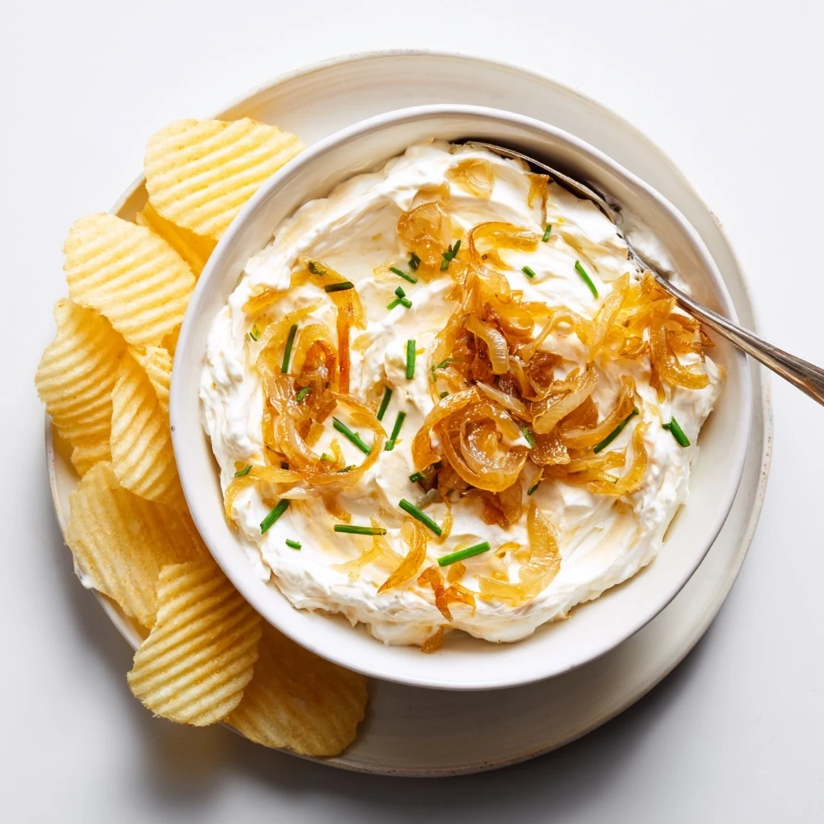 Creamy French onion dip topped with caramelized onions and fresh chives beside crispy potato chips
