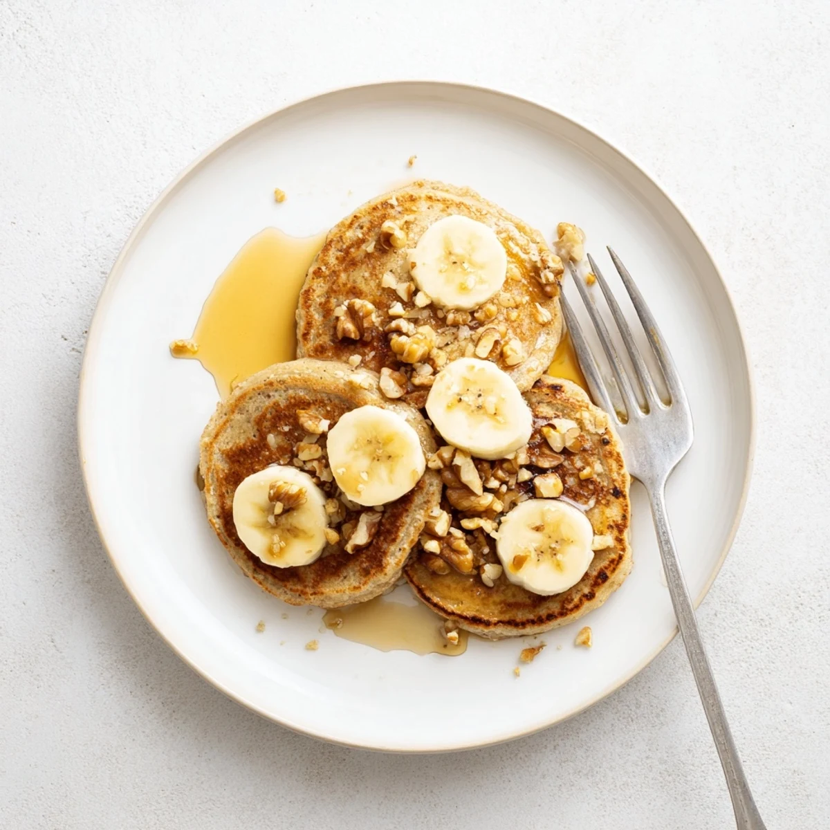 Fluffy stack of protein banana pancakes topped with fresh berries and maple syrup on a white plate