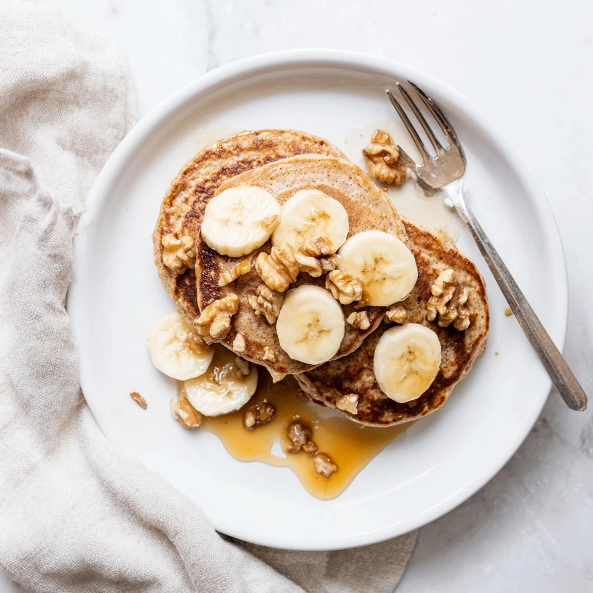 Plate of healthy protein banana pancakes drizzled with honey and sprinkled with chopped walnuts