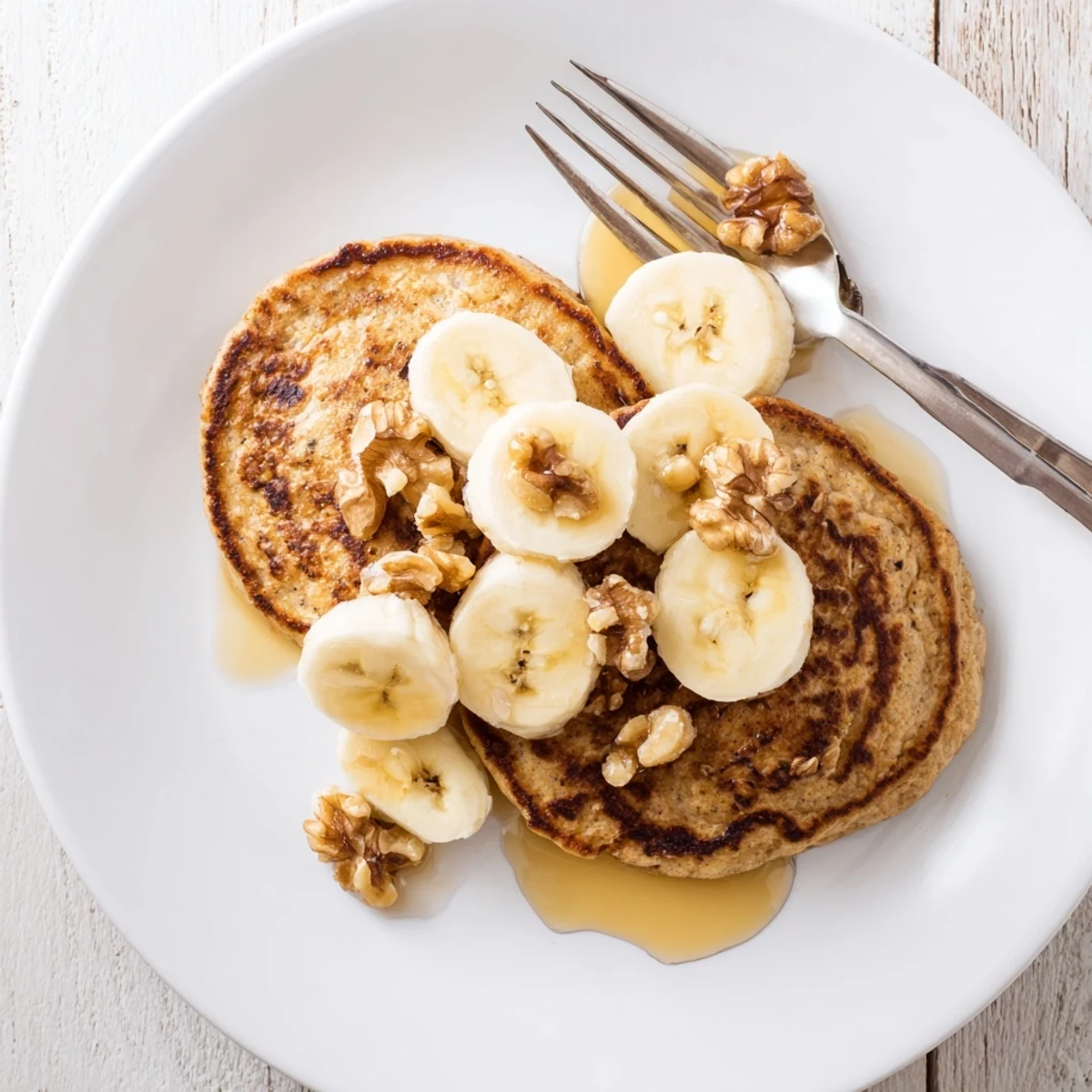Golden brown protein banana pancakes cooking on a skillet with steam rising and bubbles on surface