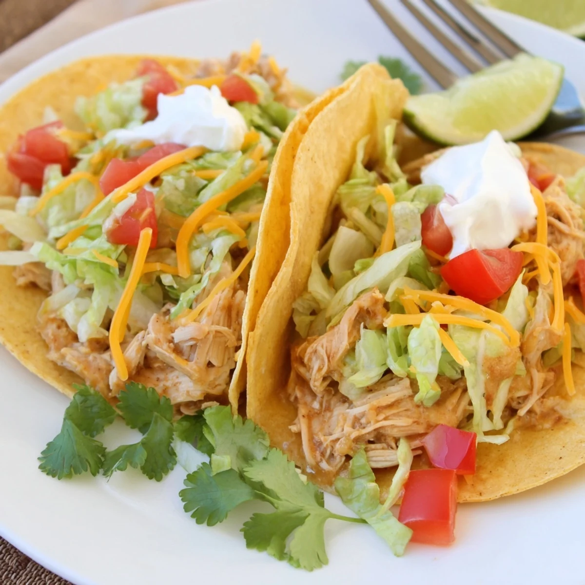 Juicy slow cooker ranch chicken tacos topped with melted cheese and fresh lime wedges