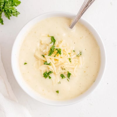 Golden roasted cauliflower and garlic swirl in this comforting Asiago Roasted Garlic Cauliflower Soup served in a rustic bowl.