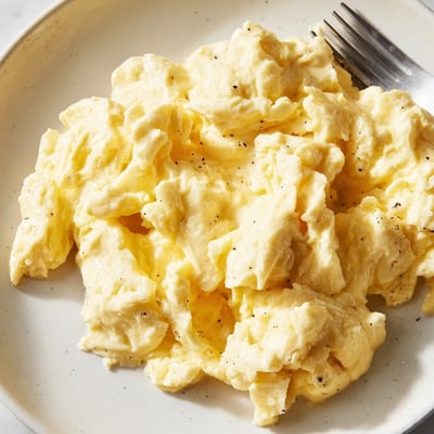 Fluffy scrambled eggs piled in a skillet with freshly cracked black pepper