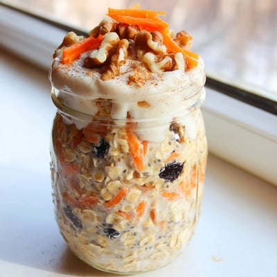 Thick spiced carrot cake overnight oats in a glass jar with raisins and pecans