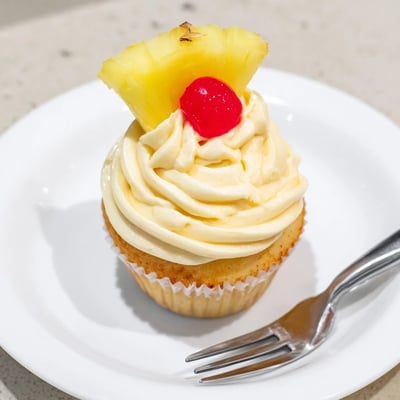 Moist pineapple-infused Dole Whip Cupcakes piped with creamy yellow frosting on a white plate